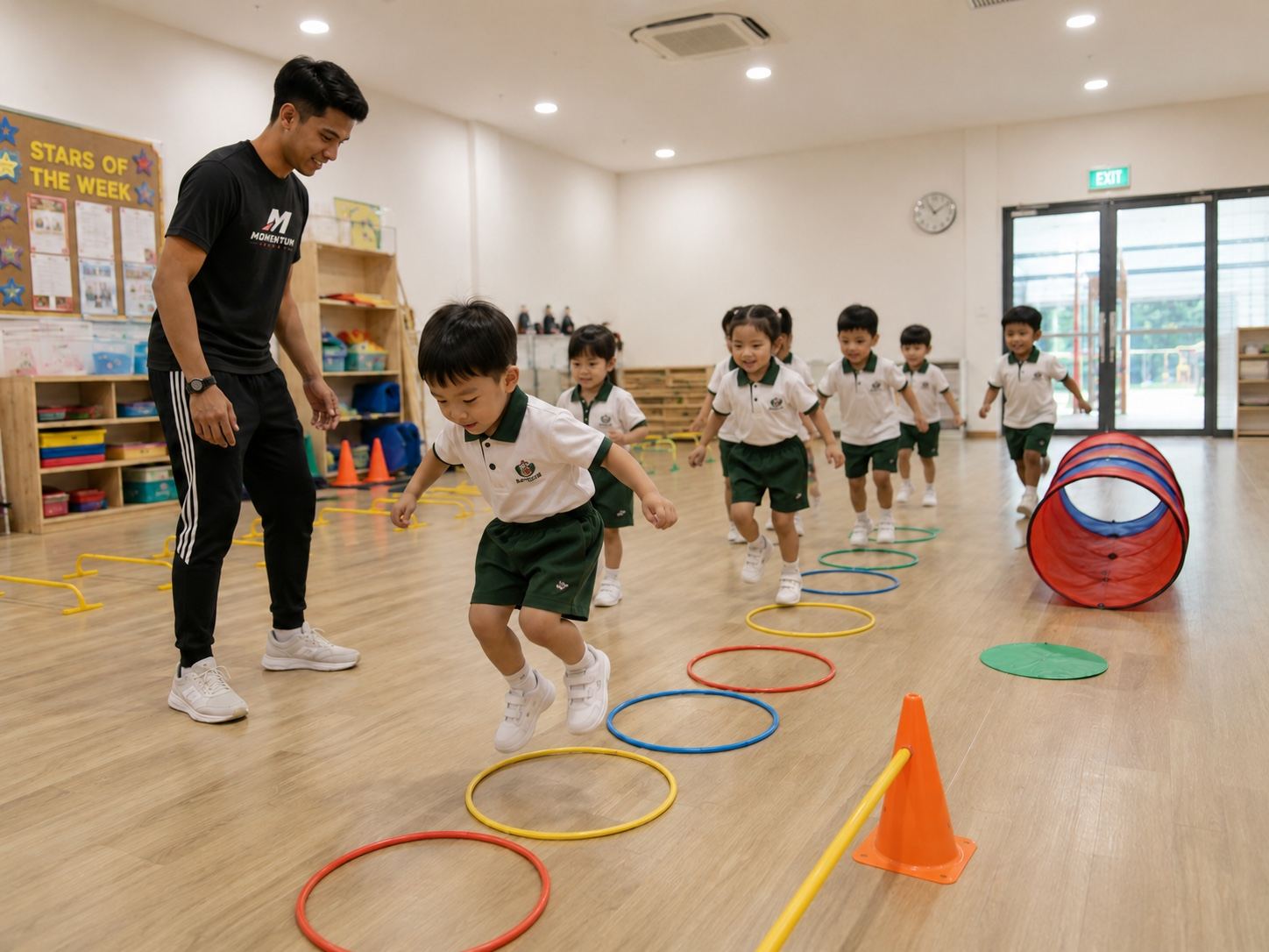 Pre-schoolers jumping through a hoop course with a Momentum Academy coach inside their centre in Singapore